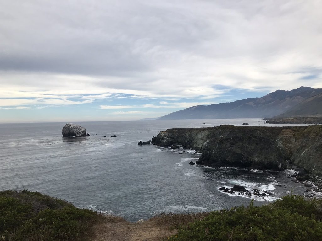 Jade Cove from the bluff, looking south down the coast toward Gorda and the Plaskett country — kelp beds offshore and Cave Rock standing in the swell.