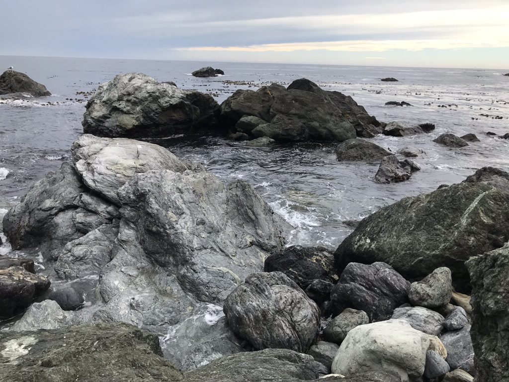Grey-green serpentine boulders pile the shore at Jade Cove — every stone a candidate until it isn't.