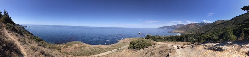Ridge-trail panorama: Highway 1 below, the point and Plaskett Rock beyond, and the coast fading south into haze.