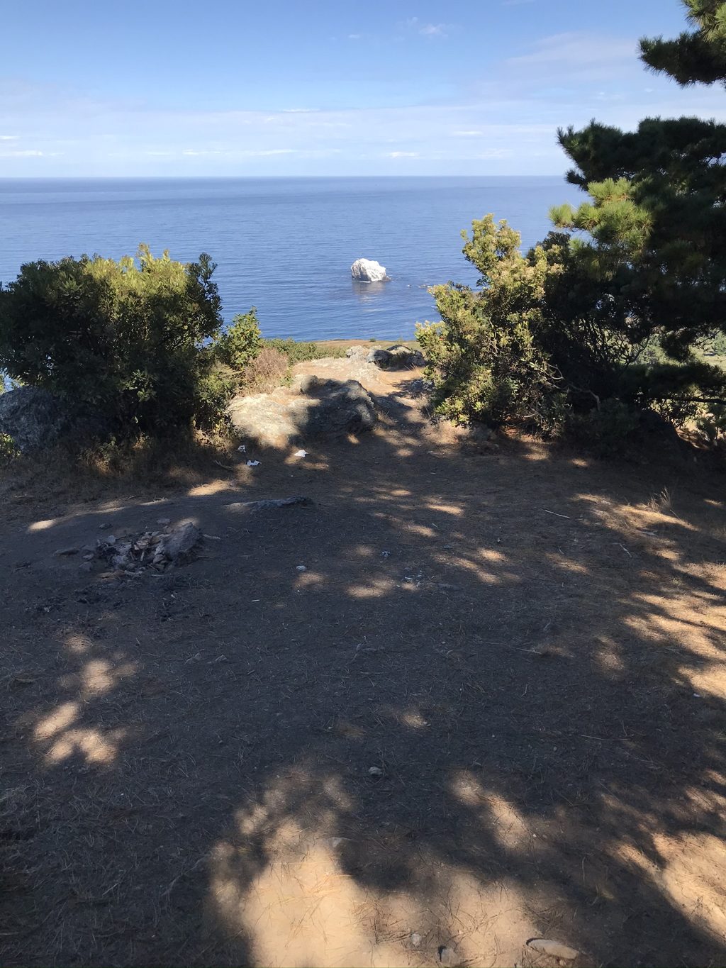 A camp clearing on Plaskett Ridge frames Plaskett Rock far below — someone's fire ring holds the best view on the coast.